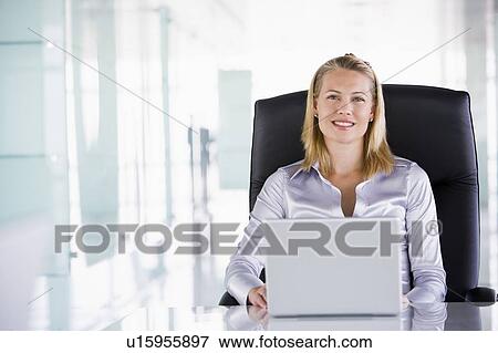 Stock Photo - Businesswoman sitting in office with laptop smiling. Fotosearch