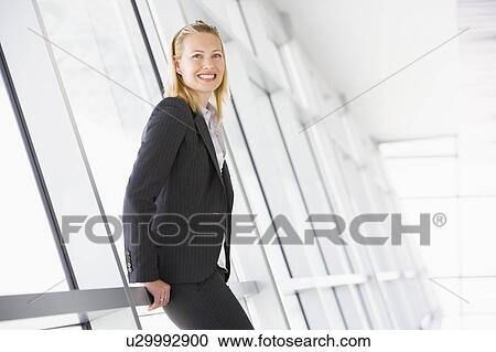 Stock Image - Businesswoman standing in corridor smiling. Fotosearch
