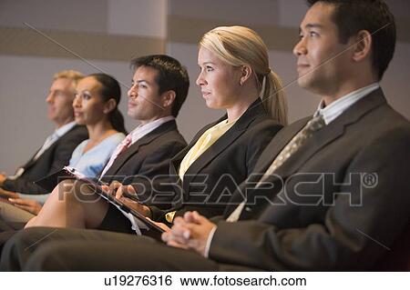 Stock Photograph - Five businesspeople sitting in presentation room with clipboards. Fotosearch