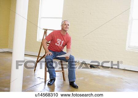Man sitting on ladder in empty space holding paper View Large Photo Image Stock Image - Man sitting on ladder in empty space holding paper. Fotosearch