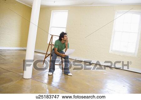 Stock Photo - Man sitting on ladder in empty space holding paper thinking. Fotosearch