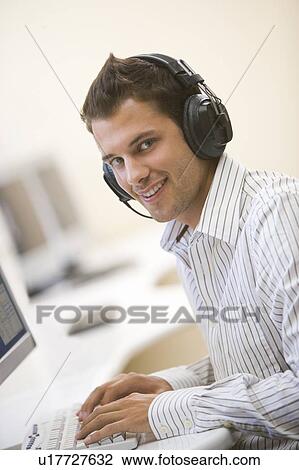 Man wearing headphones in computer room typing and smiling View Large Photo Image Stock Image - Man wearing headphones in computer room typing and smiling. Fotosearch