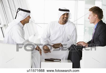 Three businessmen indoors with a laptop talking and smiling (high key/selective focus) View Large Photo Image Stock Photo - Three businessmen indoors with a laptop talking and smiling (high key/selective focus). Fotosearch