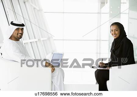 Stock Photograph - Two businesspeople indoors with a laptop smiling (high key/selective focus). Fotosearch