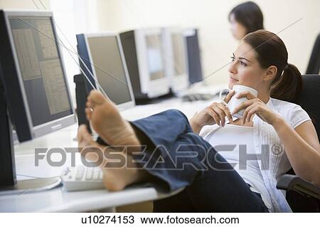 Stock Image - Woman in computer room with feet up drinking coffee. Fotosearch