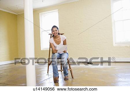 Woman sitting on ladder in empty space holding paper smiling View Large Photo Image Stock Photograph - Woman sitting on ladder in empty space holding paper smiling. Fotosearch