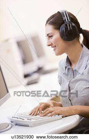 Woman wearing headphones in computer room typing and smiling View Large Photo Image Stock Image - Woman wearing headphones in computer room typing and smiling. Fotosearch