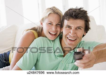 Couple in living room holding remote control smiling View Large Photo Image Stock Photograph - Couple in living room holding remote control smiling. Fotosearch