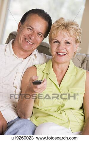 Stock Image - Couple in living room using remote control smiling. Fotosearch