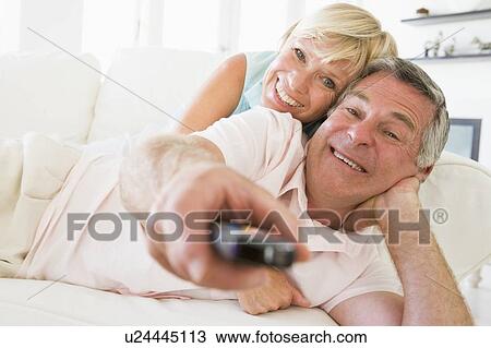 Stock Image - Couple in living room using remote control smiling. Fotosearch
