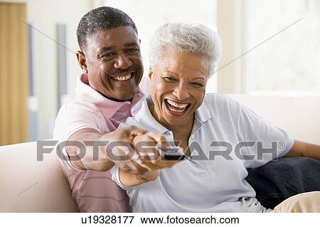 Couple in living room using remote control smiling View Large Photo Image Stock Photo - Couple in living room using remote control smiling. Fotosearch