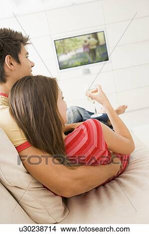 Picture - Couple in living room watching television and drinking white wine. Fotosearch