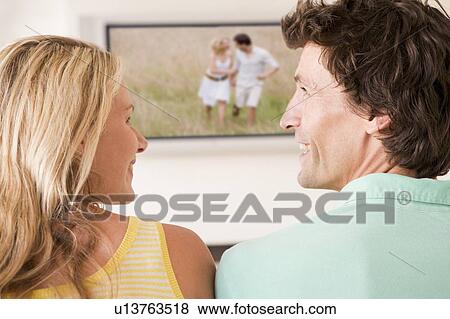 Couple in living room watching television smiling View Large Photo Image Stock Photo - Couple in living room watching television smiling. Fotosearch
