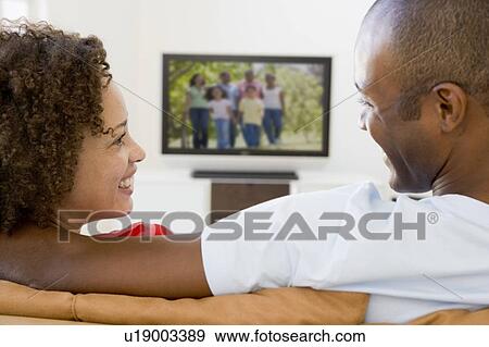 Couple in living room watching television smiling View Large Photo Image Stock Photo - Couple in living room watching television smiling. Fotosearch