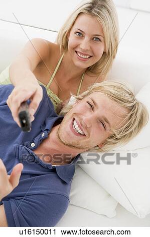 Stock Image - Couple in living room with remote control smiling. Fotosearch