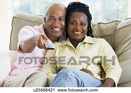 Couple relaxing in living room holding remote control and smiling View Large Photo Image Stock Image - Couple relaxing in living room holding remote control and smiling. Fotosearch