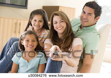 Stock Photograph - Family in living room with remote control smiling. Fotosearch
