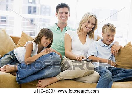 Stock Photo - Family sitting in living room with remote control smiling. Fotosearch