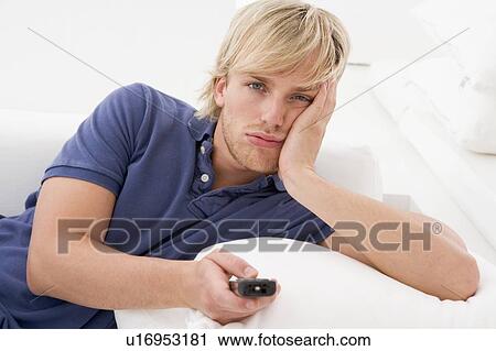 Stock Image - Man in living room holding remote control. Fotosearch