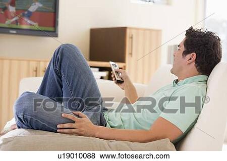 Stock Photo - Man in living room watching television. Fotosearch