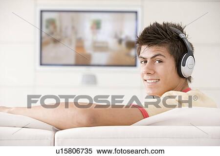 Stock Photography - Man in living room watching television and wearing headphones. Fotosearch