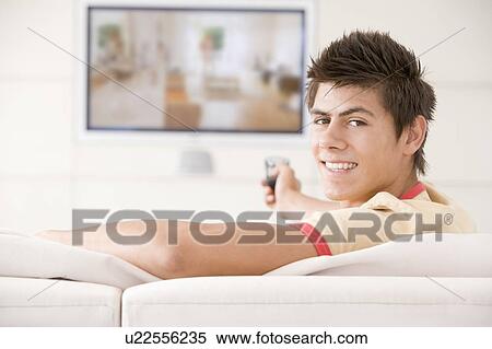 Stock Photography - Man in living room watching television smiling. Fotosearch
