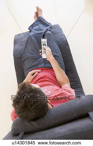 Stock Photography - Man sitting in chair using remote control. Fotosearch