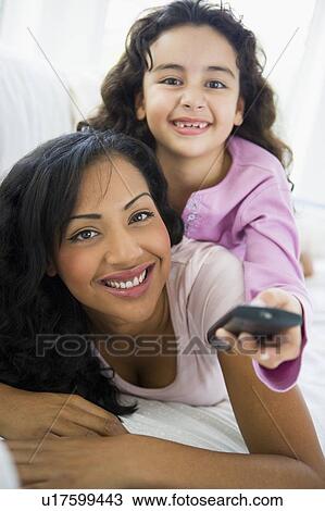 Stock Image - Mother and daughter in living room with remote control smiling (high key/selective focus). Fotosearch