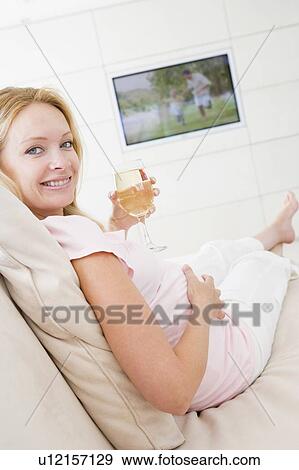 Pregnant woman watching television with glass of white wine smiling View Large Photo Image Stock Photo - Pregnant woman watching television with glass of white wine smiling. Fotosearch