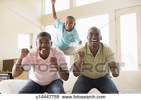 Two men and young boy in living room cheering and smiling View Large Photo Image Stock Photo - Two men and young boy in living room cheering and smiling. Fotosearch