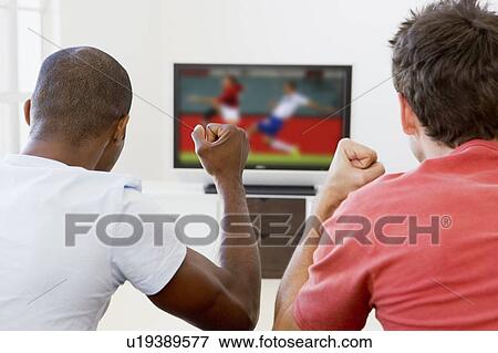 Stock Photo - Two men in living room watching television and cheering. Fotosearch