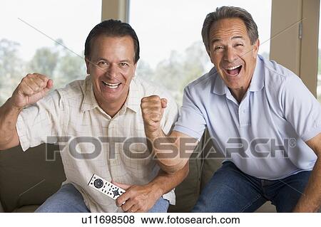 Two men in living room with remote control cheering and smiling View Large Photo Image Stock Photo - Two men in living room with remote control cheering and smiling. Fotosearch