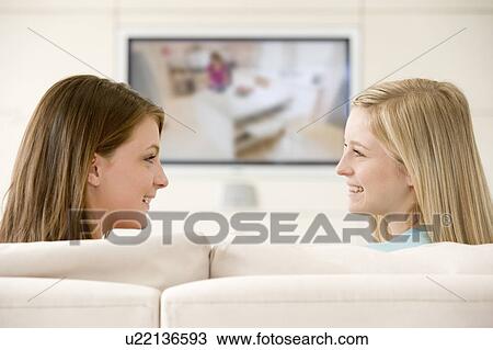 Stock Image - Two women in living room watching television smiling. Fotosearch