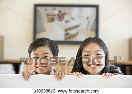 Stock Image - Two young children in living room with flat screen television smiling. Fotosearch