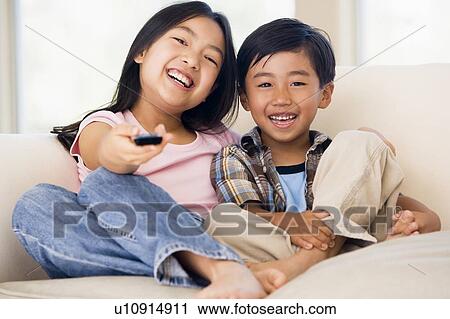 Stock Image - Two youngchildren in living room with remote control smiling. Fotosearch