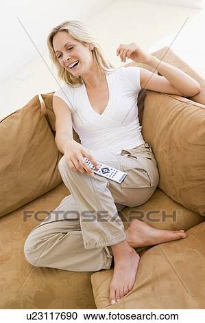 Stock Image - Woman in living room holding remote control smiling. Fotosearch