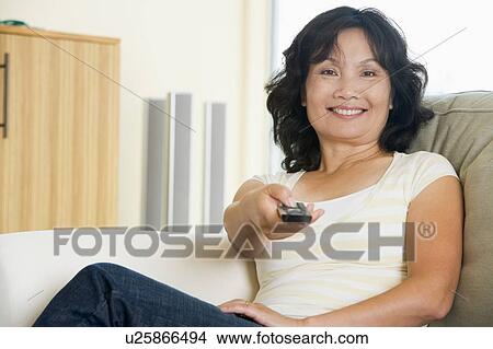 Woman sitting in living room holding remote control smiling View Large Photo Image Picture - Woman sitting in living room holding remote control smiling. Fotosearch