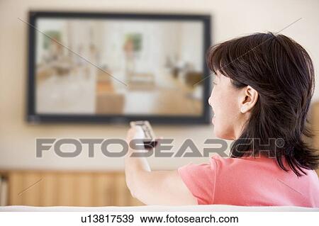 Stock Photo - Woman watching television using remote control. Fotosearch