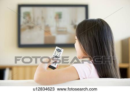 Stock Image - Young girl in living room with flat screen television and remote control. Fotosearch