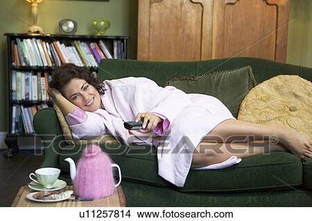 Young woman lying on sofa at home watching television View Large Photo Image Picture - Young woman lying on sofa at home watching television. Fotosearch