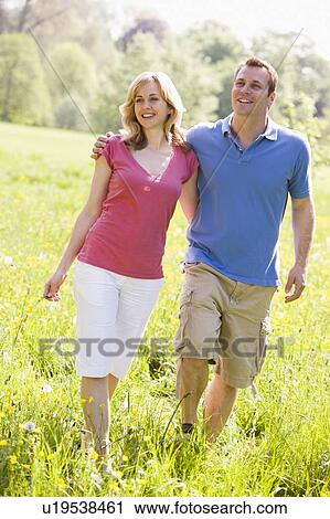 Stock Image - Couple walking outdoors holding flower smiling. Fotosearch