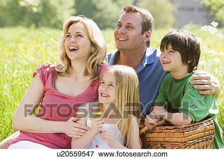 Stock Photo - Family sitting outdoors with picnic basket smiling. Fotosearch