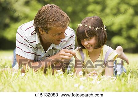 Stock Image - Father and daughter lying outdoors with flowers smiling. Fotosearch