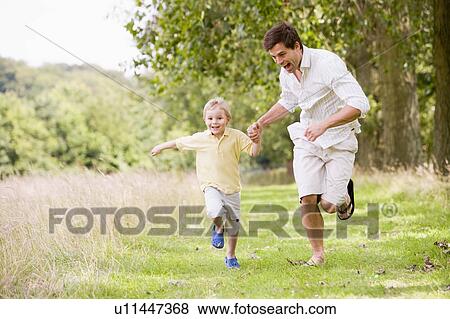 Stock Photo - Father and son running on path holding hands smiling. Fotosearch
