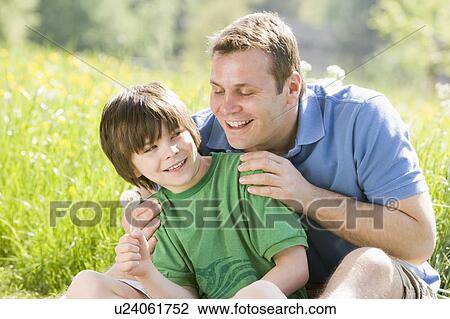 Stock Image - Father and son sitting outdoors with dandelion head smiling. Fotosearch