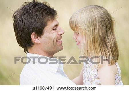 Stock Image - Father holding daughter outdoors smiling. Fotosearch
