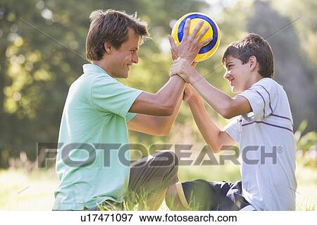Stock Photo - Man and young boy outdoors holding soccer ball and smiling. Fotosearch