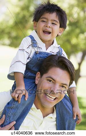 Stock Photograph - Man giving young boy shoulder ride outdoors smiling. Fotosearch