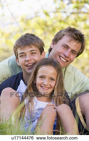 Man with two children sitting outdoors smiling View Large Photo Image Stock Photograph - Man with two children sitting outdoors smiling. Fotosearch