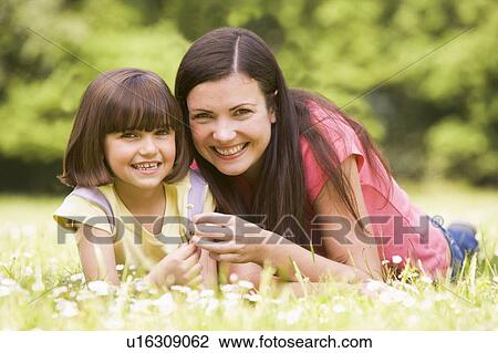Stock Image - Mother and daughter lying outdoors with flower smiling. Fotosearch